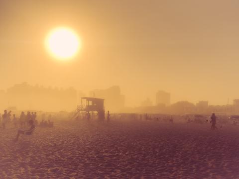 A view of a beach with all details lost into the fog. A small shack and the city lie behind the shadows