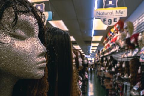 A wig in the foreground, hanging over a cracked mannequin.
